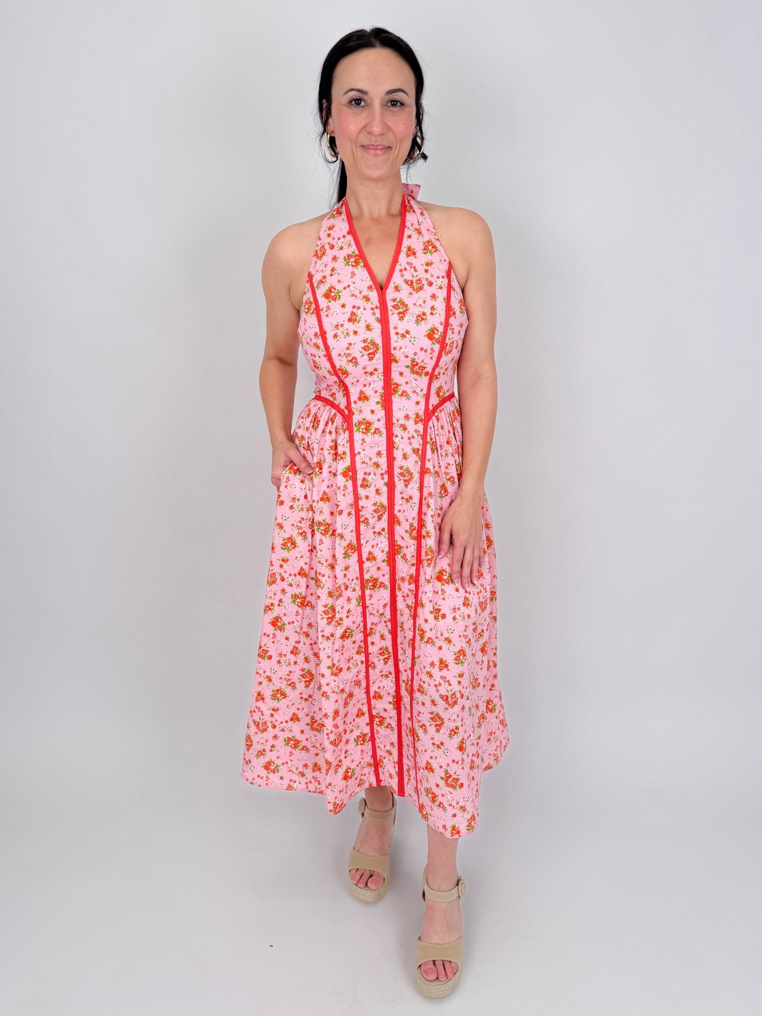 Tara Dress in pink ditsy floral print with red contrast piping, halter V neckline, fitted bodice, and full gathered midi skirt